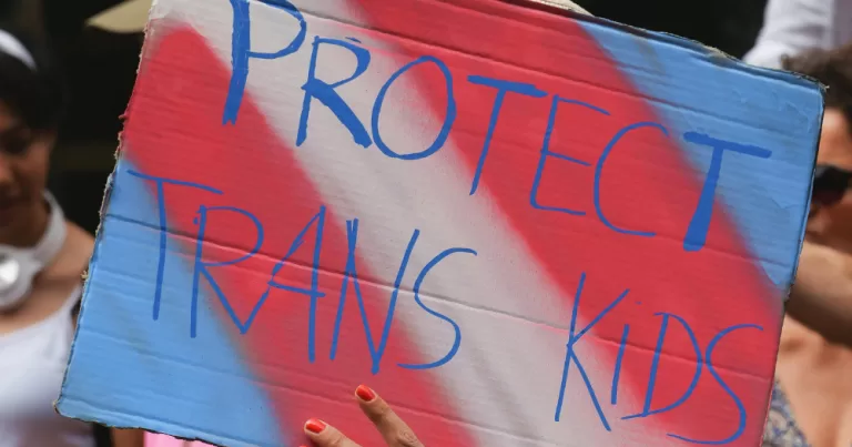 A sign reads "Protect Trans Kids"