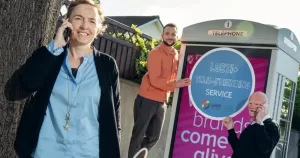 Three team members from LGBT Ireland pose with phones and advertising material promoting the Telefriending service.