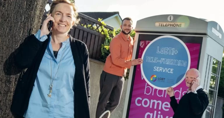 Three team members from LGBT Ireland pose with phones and advertising material promoting the Telefriending service.