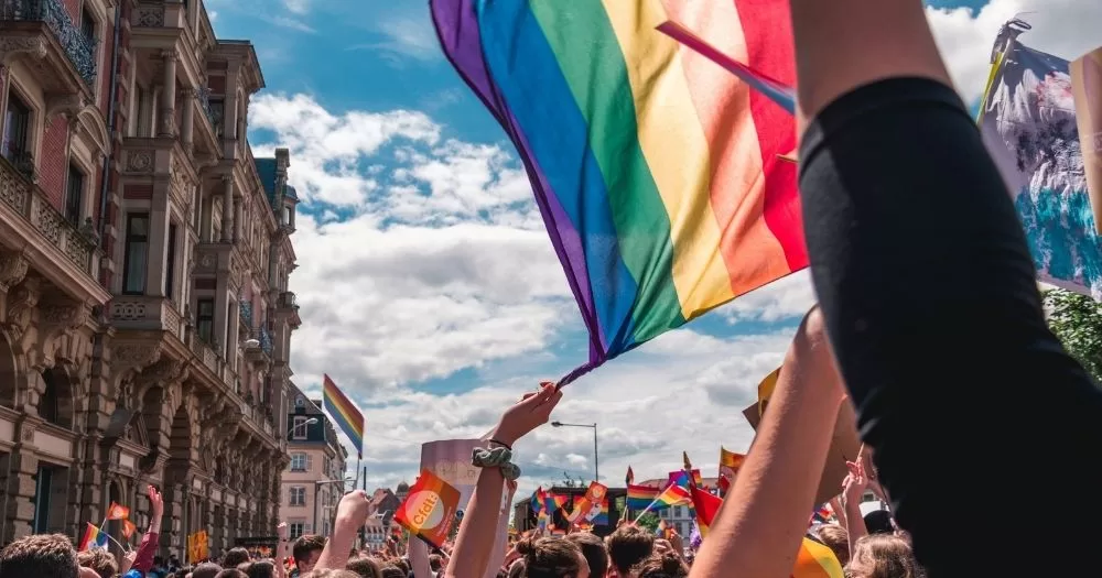 A crowd gathers for a march while someone waves a pride flag in the air.