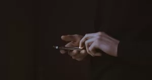 This article is about how to stay safe from sextortion on Grindr. In the photo, the hands of a person holding a phone in the dark.
