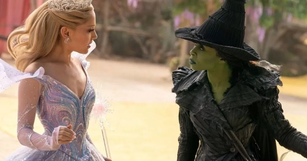 The image shows Ariana Grande and Cynthia Erivo in a still from Wicked: For Good as Glinda and Elphaba repsectively. Glinda is on the left of the image facing Elphaba, wearing a blue sparkly dress and a crown. Elphaba is dressed in a black gown and her signature pointy hat, facing Glinda on the right of the image. The image is chosen to represent the queer snubs Oscars 2026, as the film received no nominations.