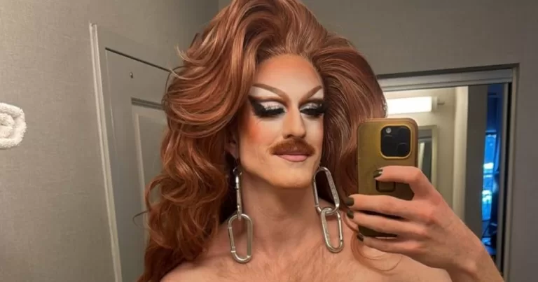 Drag queen Pattie Gonia taking a mirror selfie in full glamour. She is topless.