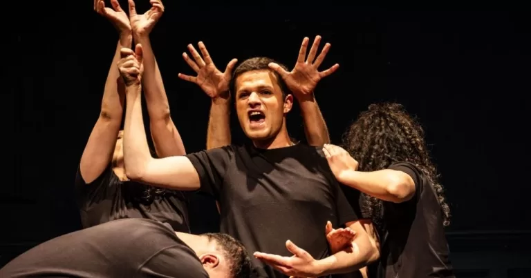 Performers from Palestine's Freedom Theatre on stage, striking a dynamic pose.