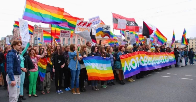 This article is about LGBTQ+ activists being targeted with Russia's undesirables law. In the photo, LGBTQ+ activists protesting and holding Pride flags, banners and signs in Russia.