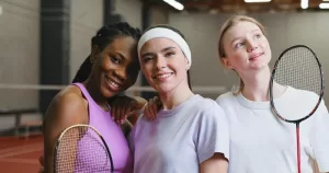 Three badminton players stand together holding their rackets. This image is being used to represent a LGBTQ+ sports day.