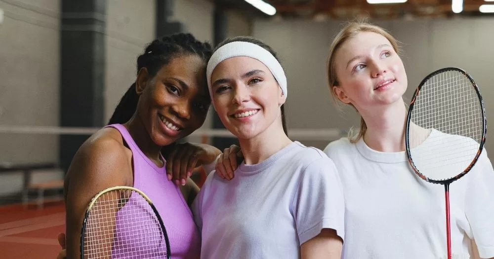 Three badminton players stand together holding their rackets. This image is being used to represent a LGBTQ+ sports day.