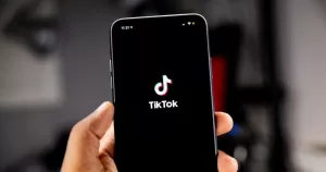 This article is about TikTok US collective sensitive information. In the photo, a hand holding a phone with the TikTok logo on the screen.