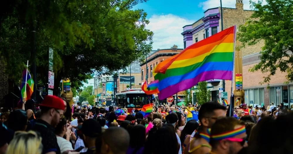 Crowds at a Pride festival, holding a large rainbow flag. This image is being used to accompany and article about Cork Community Pride.