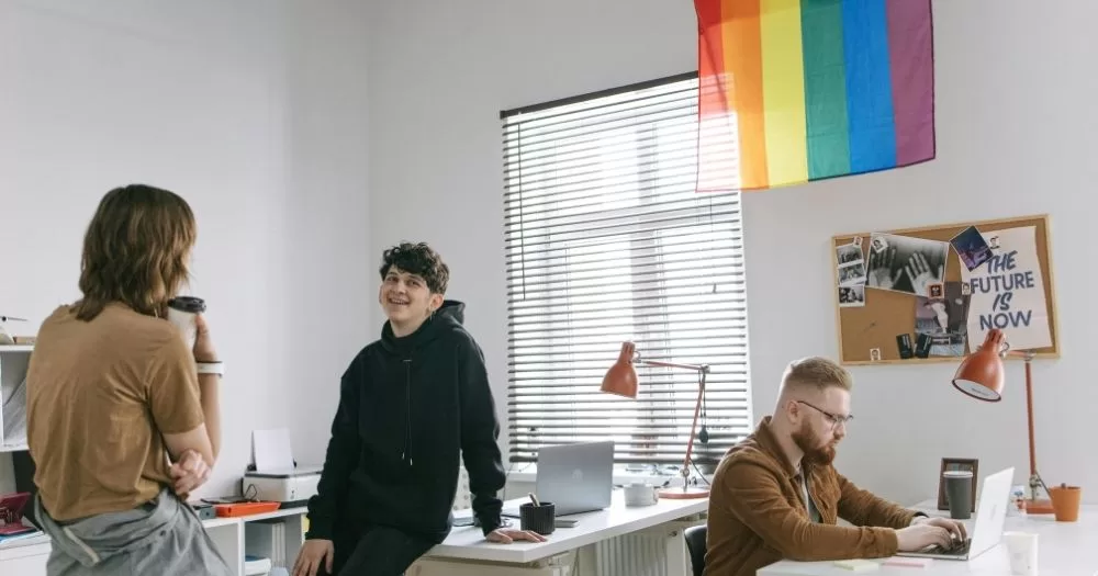 DEI rollback study. Three people in a bright office with a pride flag on the wall. The vibes are nice.
