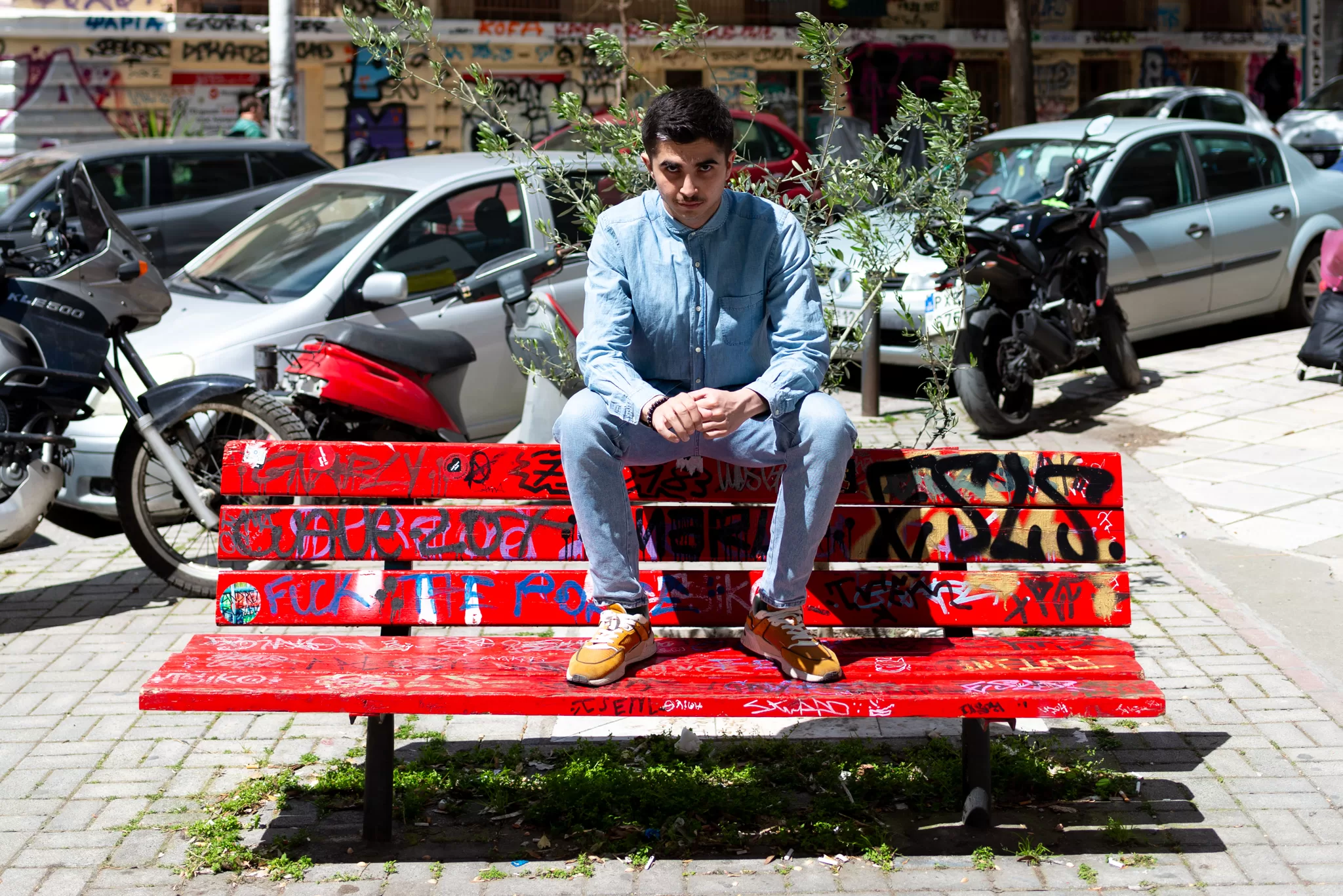 A man sits on top of a red bench in a Balkan city.