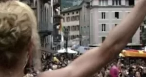 A still from the film The Parade: Our History. It shows a person from behind raising their arm over a crowd of people below.