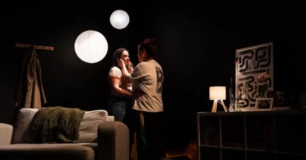 Two actors embrace each other on stage as they perform In Vitro.