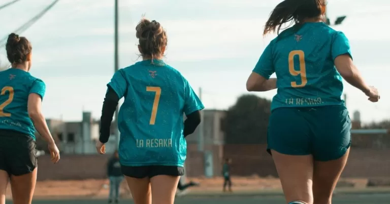 A trio of women running together on a sports field. They are in a sports uniform.