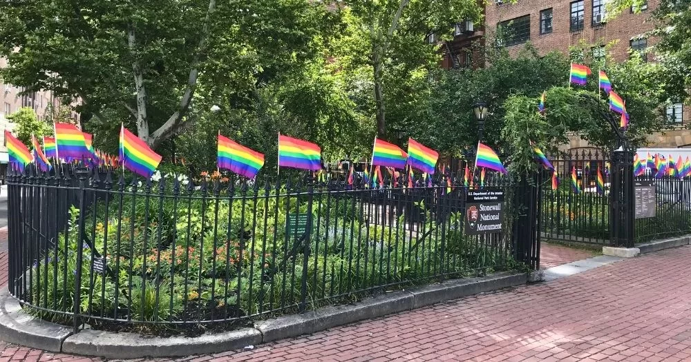 Photo of the Stonewall National Monument, where the Trump administration had the Pride flags removed, with a series of Pride flags flowing on the fence.