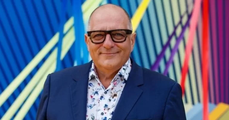 Irish presenter Hugh Wallace smiling at the camera while wearing a blue suit with a colourful background.