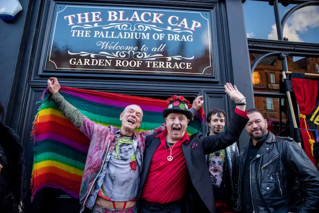 People stand outside The Black Cap with their arms around one another.