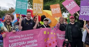 The Rainbow Project team pose at a Pride event holding banners and posters.
