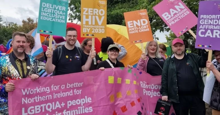 The Rainbow Project team pose at a Pride event holding banners and posters.