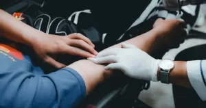 This article is about blood donation and LGBTQ+ people. In the photo, the arm of a person who is donating blood and a the hand of a nurse.