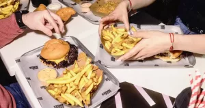 Close-up of hands eating burgers and chips from Dash Burger