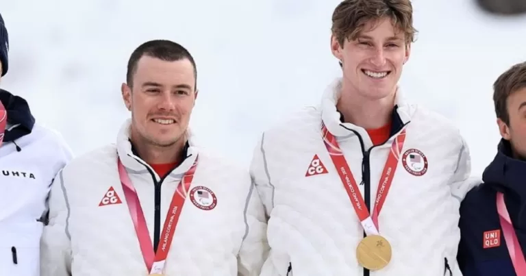 Jake Adicoff and his guide Reid Goble stand at the podium with gold medals around their necks.