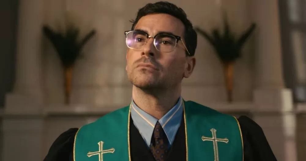 Actor Dan Levy dressed at a pastor, standing at an alter.