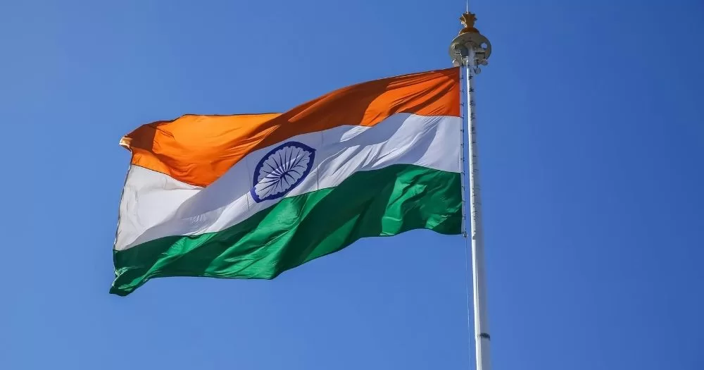 An Indian flag waving in the sky. This image is being used to represent an article about India's parliament passing a bill that restricts who can identify as trans.