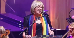 Philippa Ryder, Dublin Pride 2026 Grand Marshall, stands at a microphone, addressing an audience while wearing a rainbow scarf.