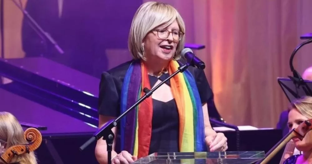 Philippa Ryder, Dublin Pride 2026 Grand Marshall, stands at a microphone, addressing an audience while wearing a rainbow scarf.