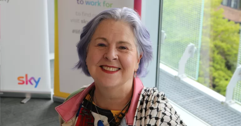Lynne Tracey smiles for a picture at an event. She is wearing a pink collared shirt.