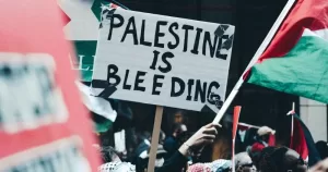 A pro-Palestine protest. A banner reads "Palestine is bleeding". A Palestinian flag flies.