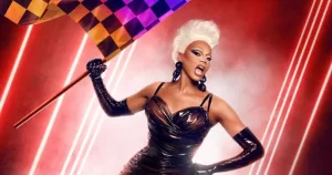 RuPaul holds up an orange, pink, and purple checkered flag in front of a smoky, red background with lasers for the All Stars 11 promo.