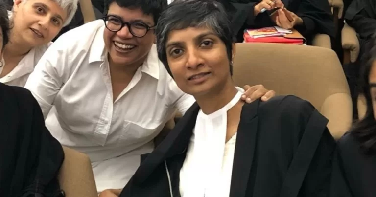 Menaka Guruswamy, India's first openly LGBTQ+ MP, sits down and is surrounded by colleagues.