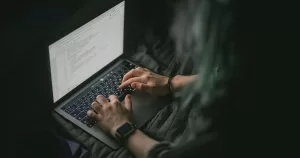 A person is on a laptop on bed. This image is being used to represent sexual extortion.