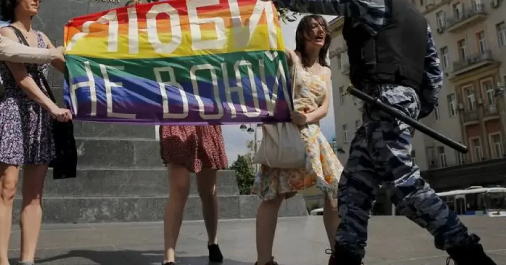 An officer rips a Pride flag away from protesters, this article covers Russian extremist labels on LGBTQ+ groups.
