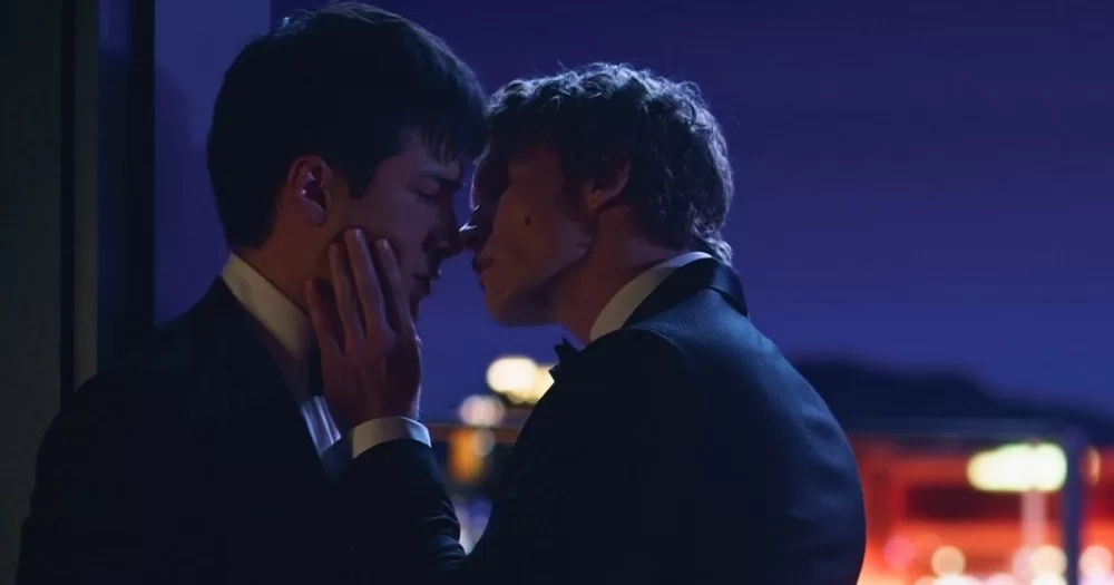 The two protagonists of Heated Rivalry, which recently won a prestigious award, as they're almost kissing on a balcony at night.