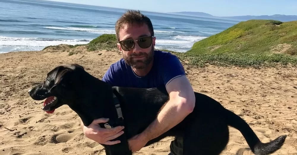Jacob Tierney hugs his dog, a black lab mix, on a beach on a sunny day. Jacob Tierney has been praised online for being open about his HIV status.
