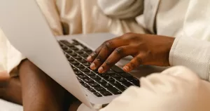 This article is about LGBTQ+ support groups. The image shows a person sitting with their laptop in their lap.
