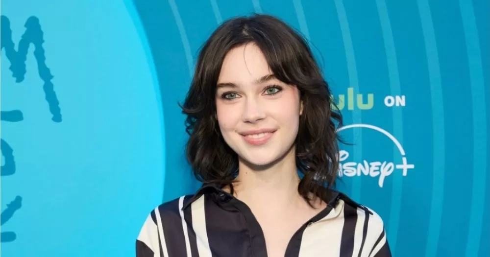 Non-binary actor Vaughan Murrae smiles in front of a blue backdrop advertising Malcolm in the Middle: Life's Still Unfair.