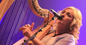 Moya Brennan on stage singing and playing the harp.