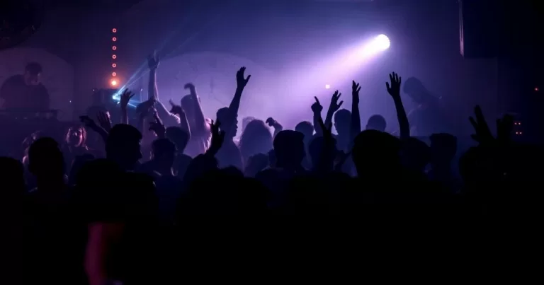 This article is about Queer Rave, taking place in Dublin. In the image, a crowd dancing in a club with purple lighting.