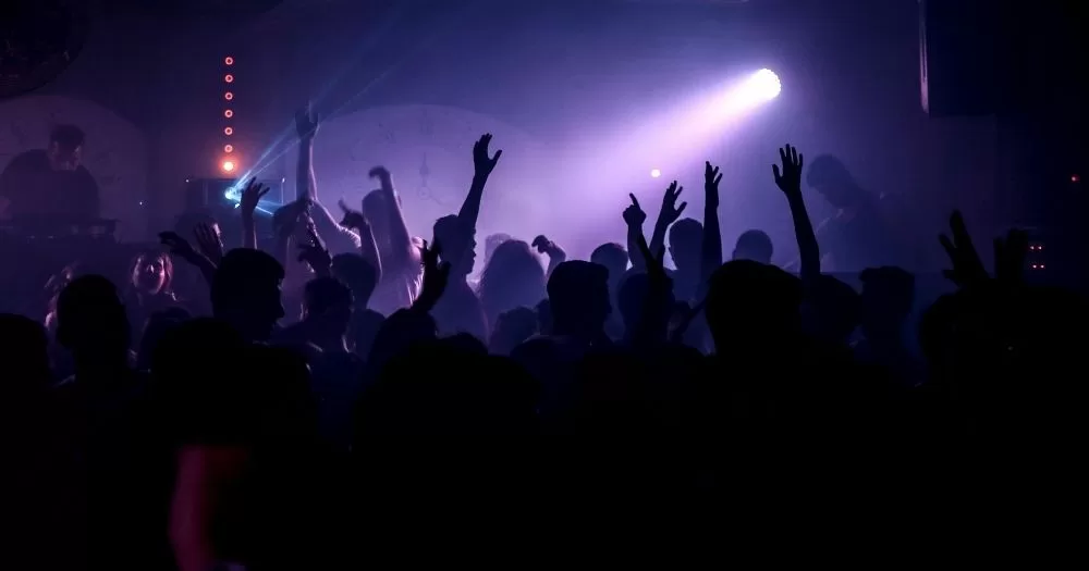 This article is about Queer Rave, taking place in Dublin. In the image, a crowd dancing in a club with purple lighting.