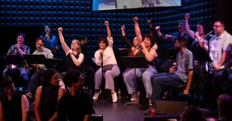 Members of EPIC Players' theatre company sit on a stage and raise their fists during a performance.