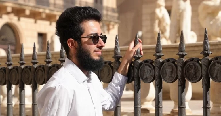 Arian Mirzarafie-Ahi, a Romanian trans man, stands next to a gate and looks off into the distance.