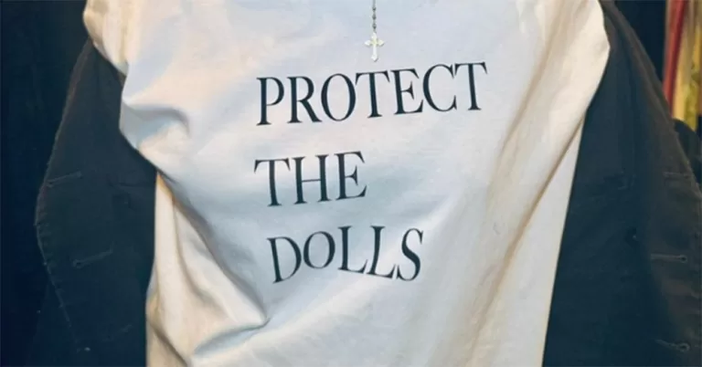 A close up of a white t-shirt with the trans term "Protect the dolls" in black writing.