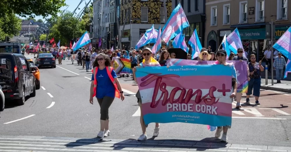 People marching in the streets carrying a banner that reads Trans+ Pride Cork.