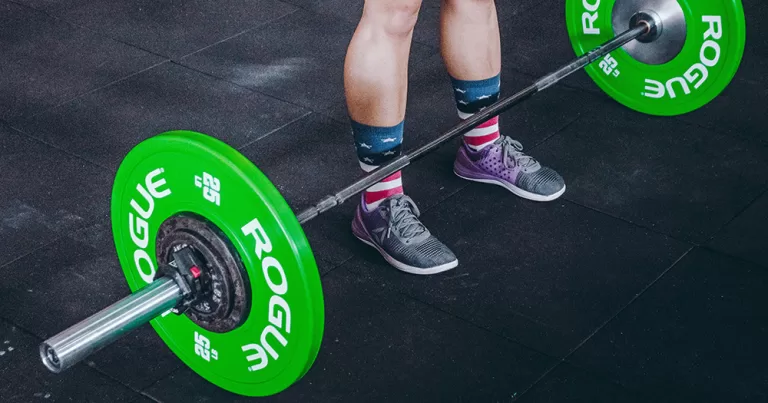 The photo shows a person's feet and a barbell used for powerlifting.