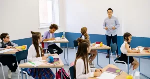 A teacher stands at the front of a classroom teaching a group of students.