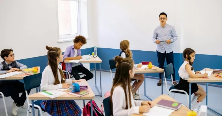 A teacher stands at the front of a classroom teaching a group of students.